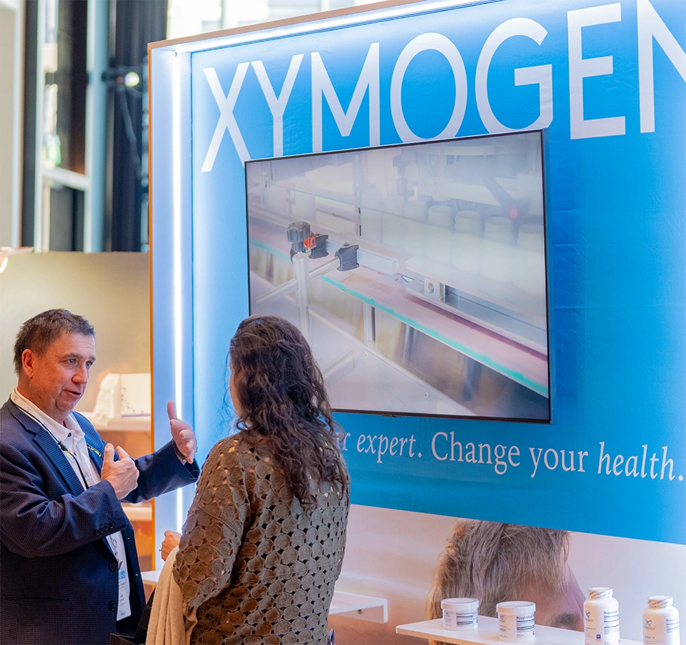 Conference attendees conversing in front of the XYMOGEN booth